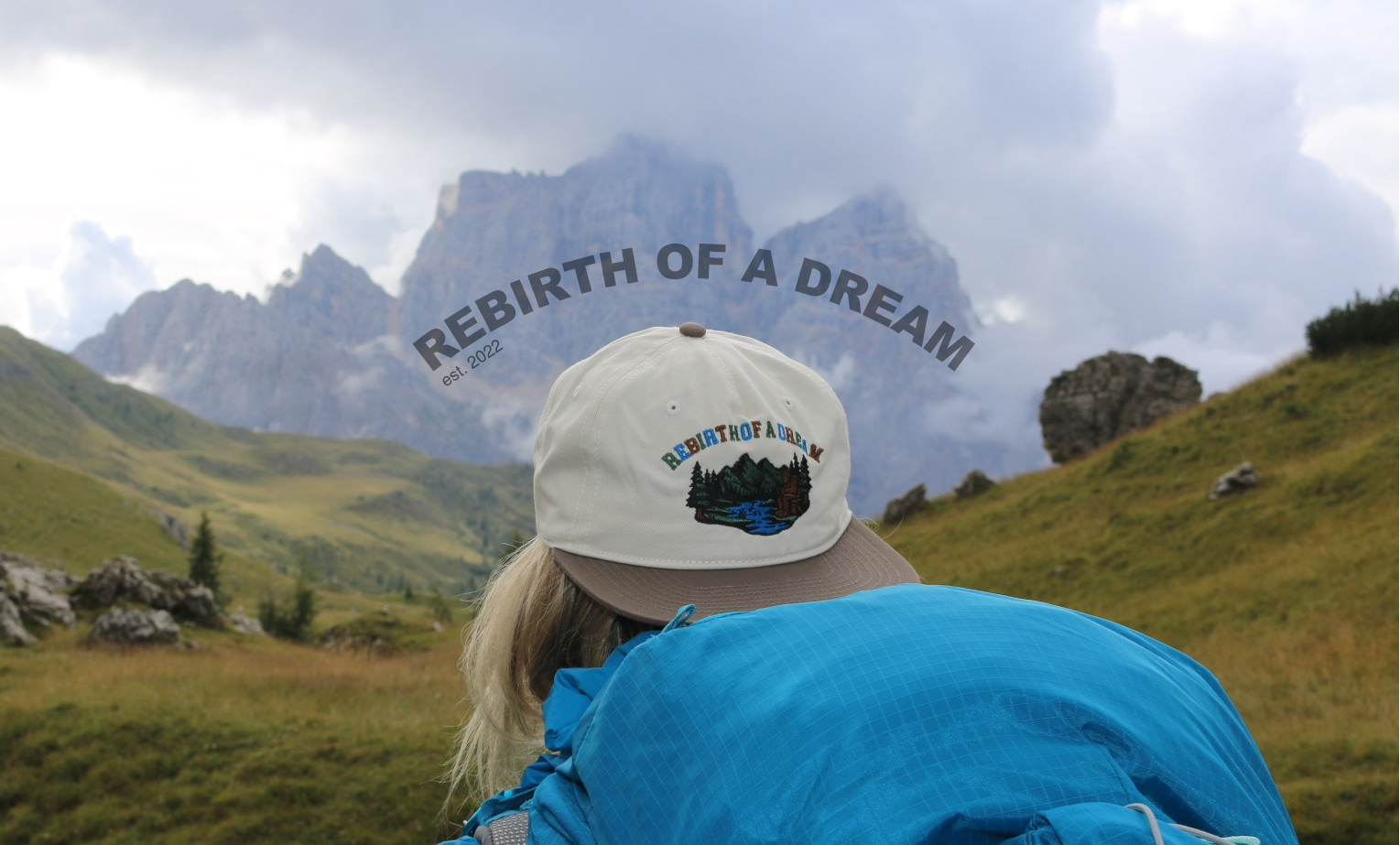 Person wearing a 'Rebirth of a Dream' cap in a mountainous landscape